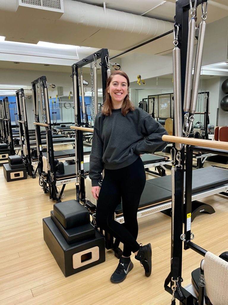 Pilates Instructor Meg DiRuggiero Standing In Front of Reformer Machines