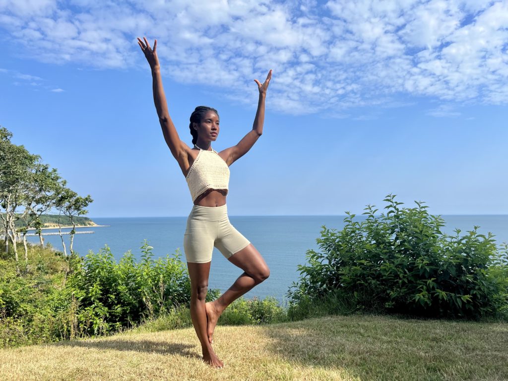 Genesha Michelle Doing a Yoga Pose Outside in Front Of Water